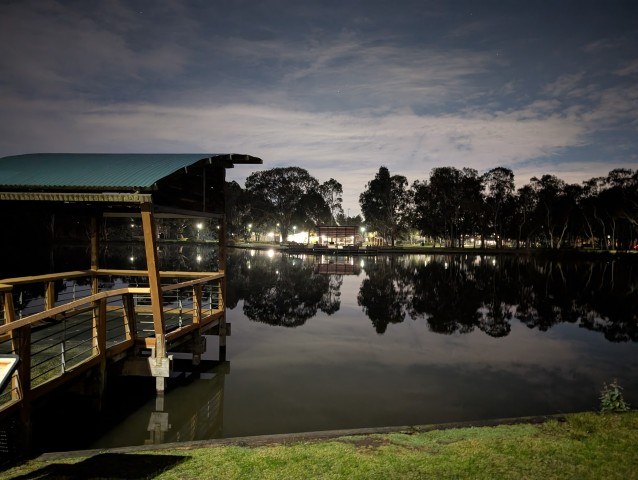 Night view across the lake at Banjo Paterson Park in Lynbrook with reflections and a covered viewing deck